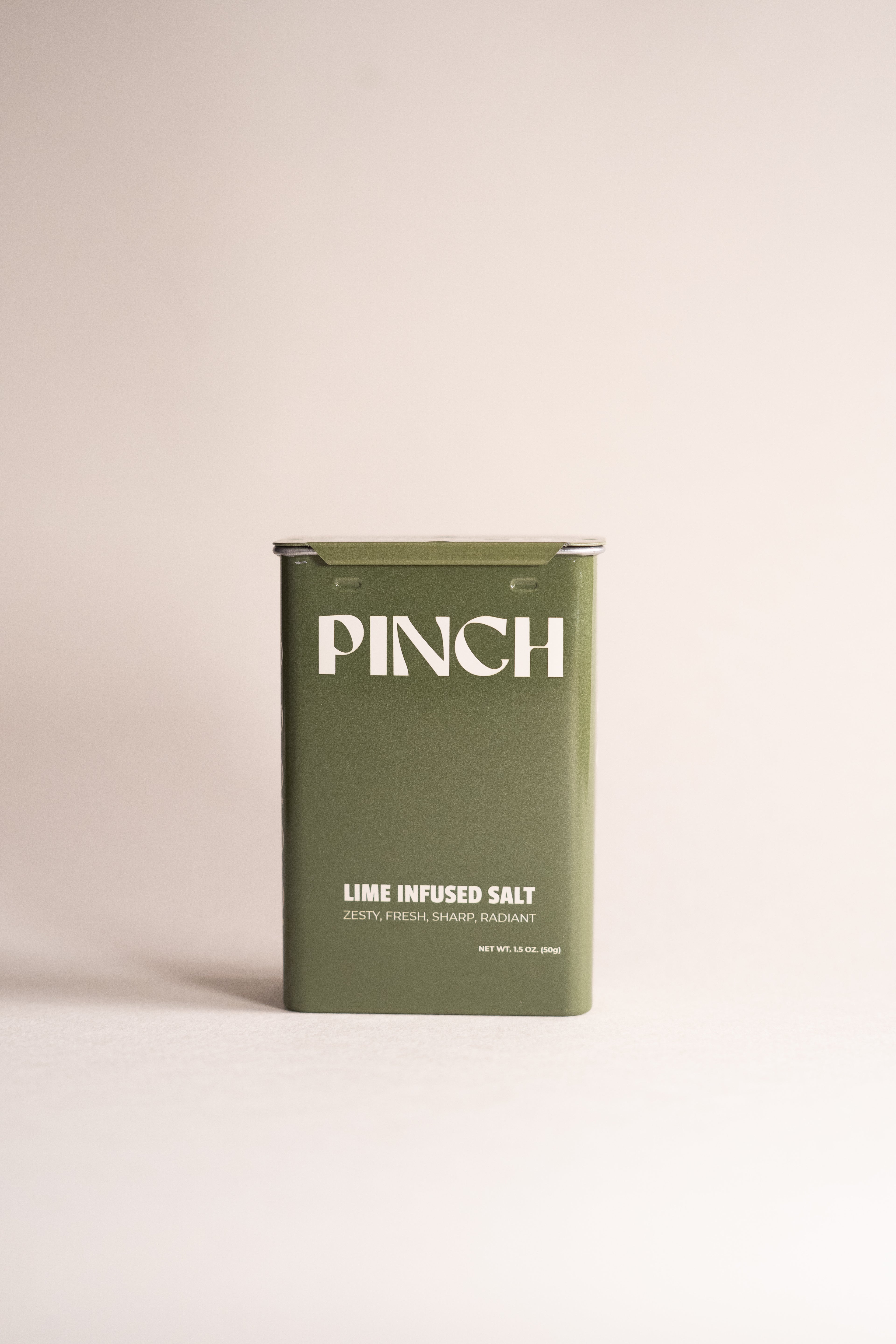 Green container of 'PINCH' lime infused salt on a beige background