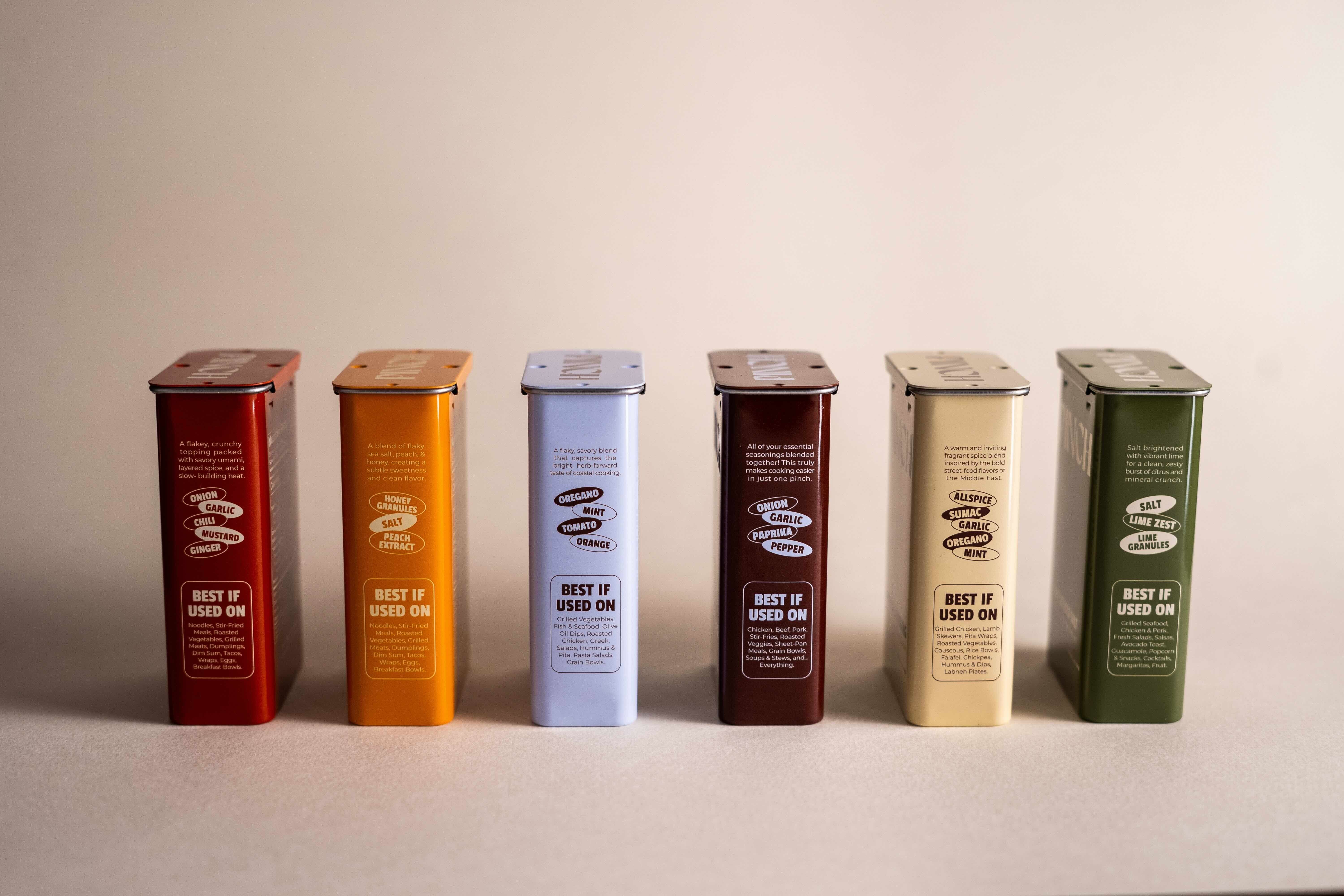  six pinch seasoning tins lined up (side view) in a straight line. Tins portray each pinch seasoning flavor 