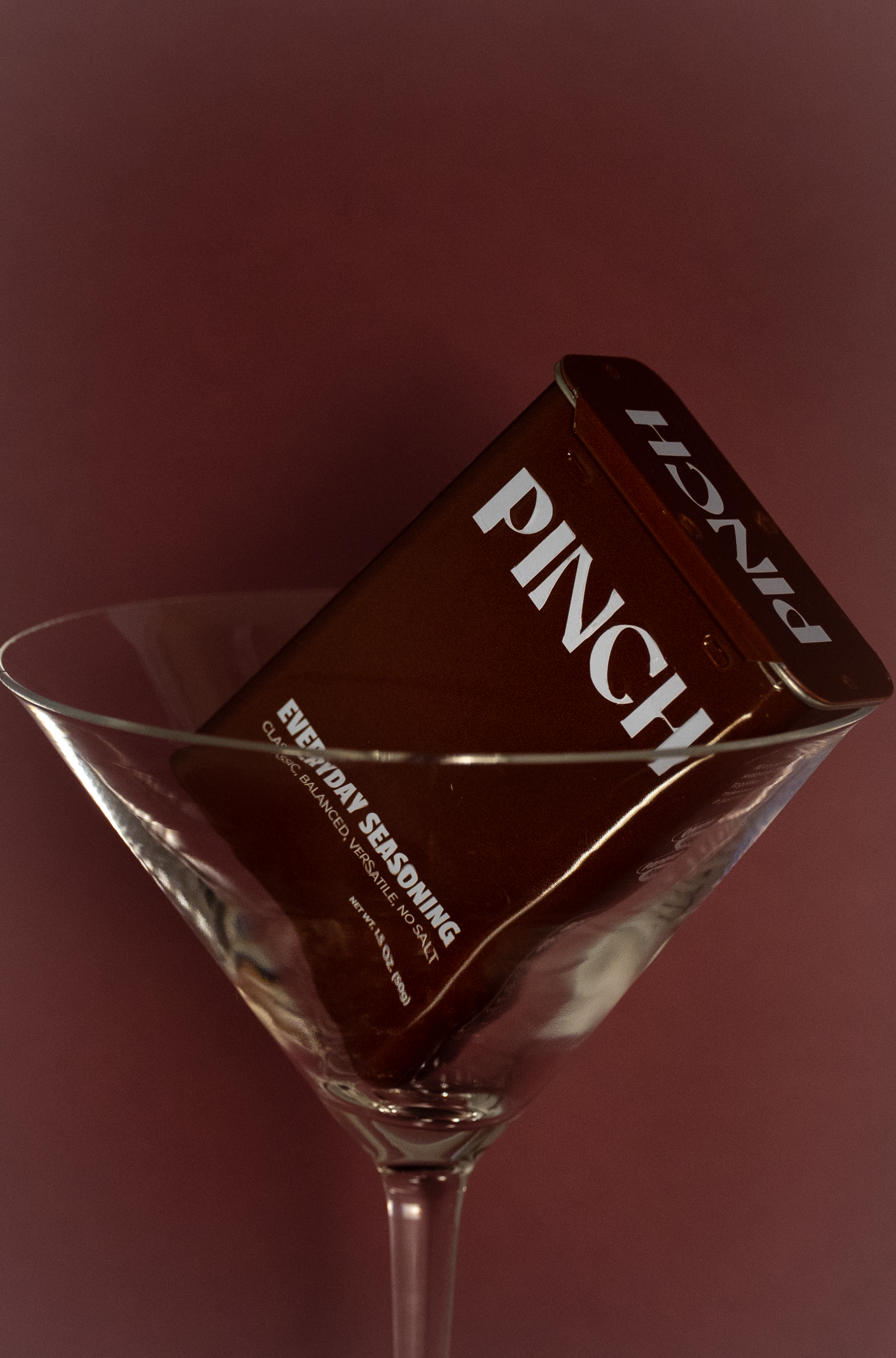 A PINCH seasoning can in a martini glass against a dark background